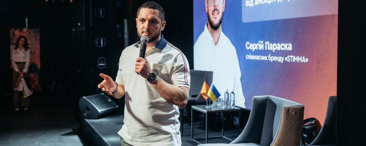 Співзасновник бренду Stimma стоїть на сцені з мікрофоном у руках, позаду великий екран.
