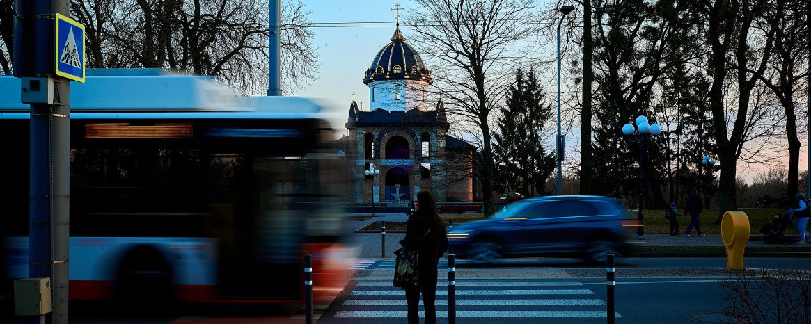 Динамічна вулиця з громадським транспортом, людьми та церквою на горизонті.