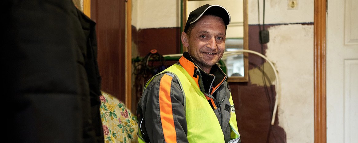 Чоловік у спецодязі та кепці сидить у невеликій сторожовій комірчині.