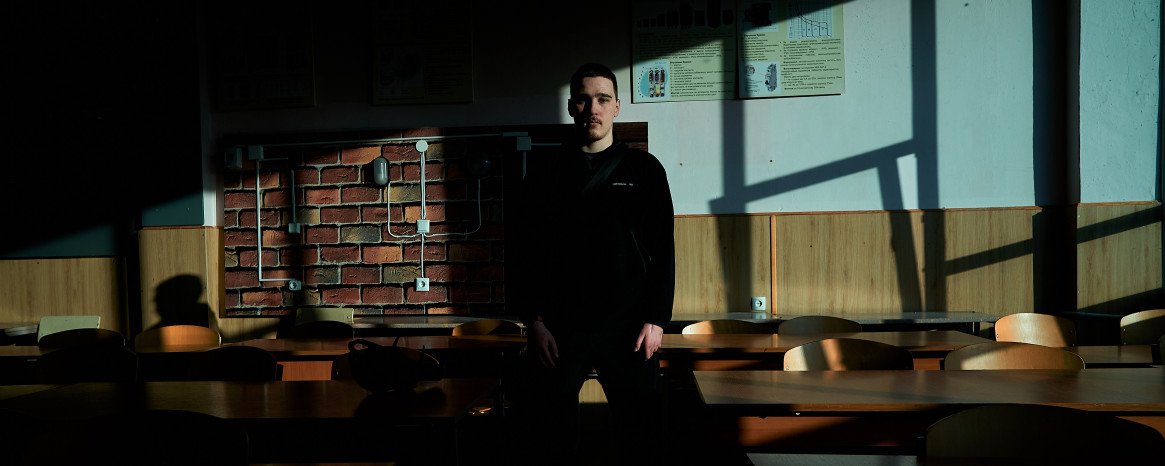 У центрі класної кімнати з партами стоїть хлопець.