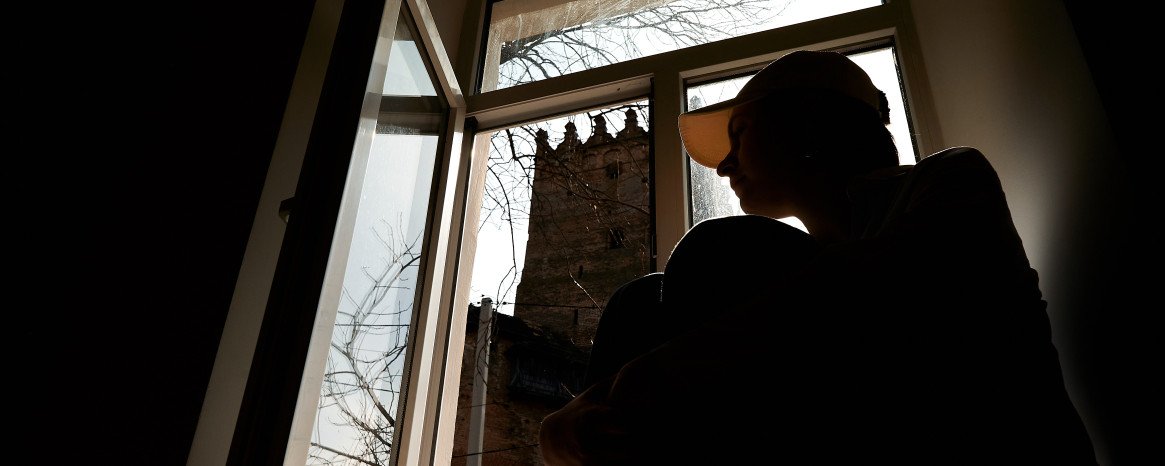 Силует дівчини на на підвіконні з видом на Луцький замок з вікна.