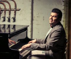 Усміхнений чоловік у картатому костюмі грає на піаніно