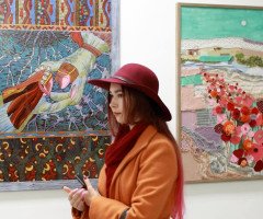 Дівчина в червоному капелюсі та помаранчевому пальто на тлі картин.