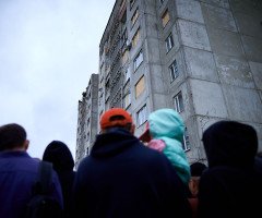 Люди стоять навпроти зруйнованої багатоповерхівки.