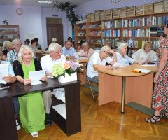 Люди сидять за столами в приміщенні бібліотеки, слухають лекторку