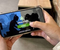 Жіноча рука тримає мобільний телефон, на якому зображено початковий екран застосунку LifesaverSIM.