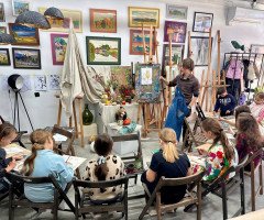 діти сидять під час уроку малювання в артстудії і дивляться на вчителя з мольбертом