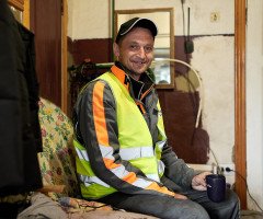 Чоловік у спецодязі та кепці сидить у невеликій сторожовій комірчині.