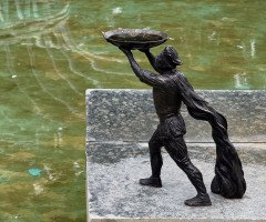 Скульптура чоловіка у плащі з чашею в руках.