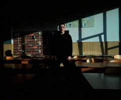 У центрі класної кімнати з партами стоїть хлопець.