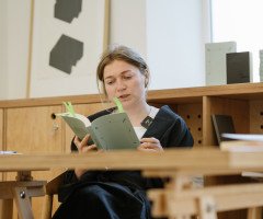 Жінка читає книгу сидячи за столом.