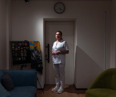 Жінка в білому медичному костюмі в темній кімнаті.