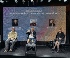 Чотири людини сидять на стільцях на сцені, позаду них екран.