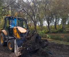 трактор згрібає рослинні залишки і сміття на території зеленої зони біля водного каналу