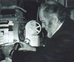 Сивий чоловік біля стосу книг з кіноплівкою в руках