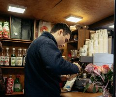 Всередині невеликого кава-кіоску хлопець біля кавомашини готує капучино.