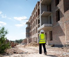 Людина на будівництві йде вздовж стіни у жилеті та будівельній касці.
