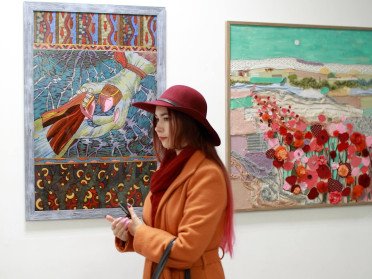 Дівчина в червоному капелюсі та помаранчевому пальто на тлі картин.