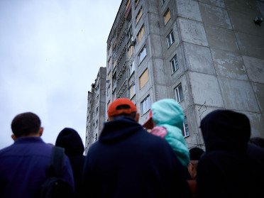 Люди стоять навпроти зруйнованої багатоповерхівки.