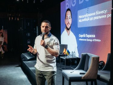 Співзасновник бренду Stimma стоїть на сцені з мікрофоном у руках, позаду великий екран.