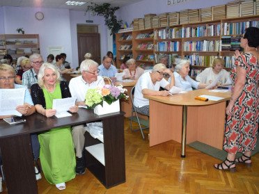 Люди сидять за столами в приміщенні бібліотеки, слухають лекторку