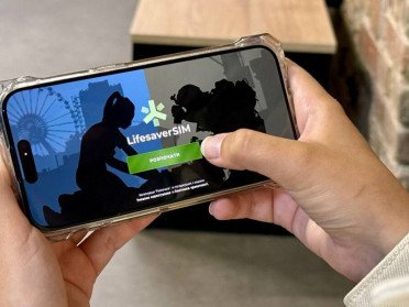 Жіноча рука тримає мобільний телефон, на якому зображено початковий екран застосунку LifesaverSIM.