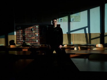 У центрі класної кімнати з партами стоїть хлопець.