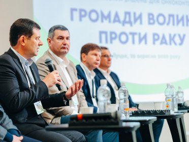 Чоловіки з мікрофонами на тлі банеру «Громади - Волині проти раку».