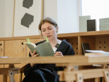 Катерина Яковленко презентувала книгу «Донбас як метафора». Жінка читає книгу сидячи за столом.