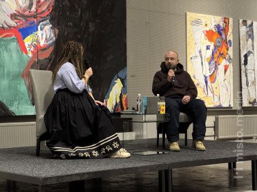 Двоє людей сидять на кріслах на сцені.