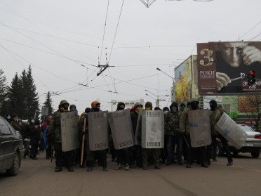 Чоловіки в балаклавах, касках та з міліцейськими металевими щитами стоять на проїжджій частині проспекту Волі у Луцьку.
