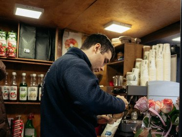 Всередині невеликого кава-кіоску хлопець біля кавомашини готує капучино.