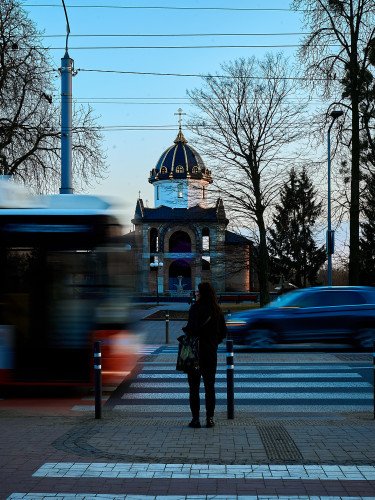 Динамічна вулиця з громадським транспортом, людьми та церквою на горизонті.