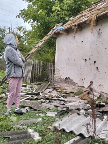 жінка стоїть біля стіни будинку, пошкодженого уламками