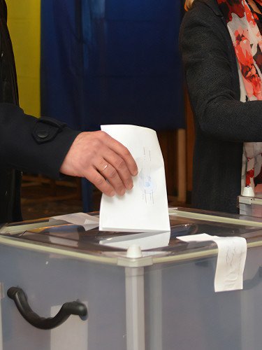 Чоловік і жінка кидають бюлетені в урни для голосування.