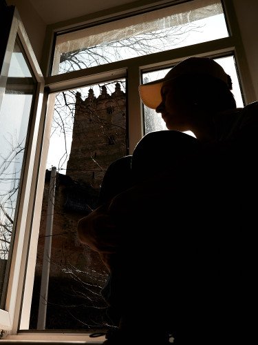 Силует дівчини на на підвіконні з видом на Луцький замок з вікна.