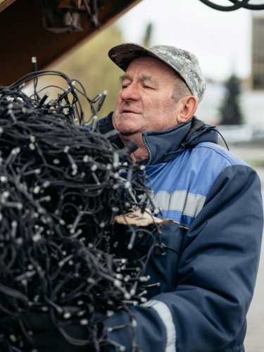 Літній чоловік у спецодязі несе оберемок гірлянд.