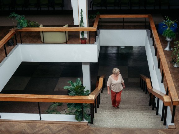 Сходовий майданчик, по якому підіймається світловолоса жінка.