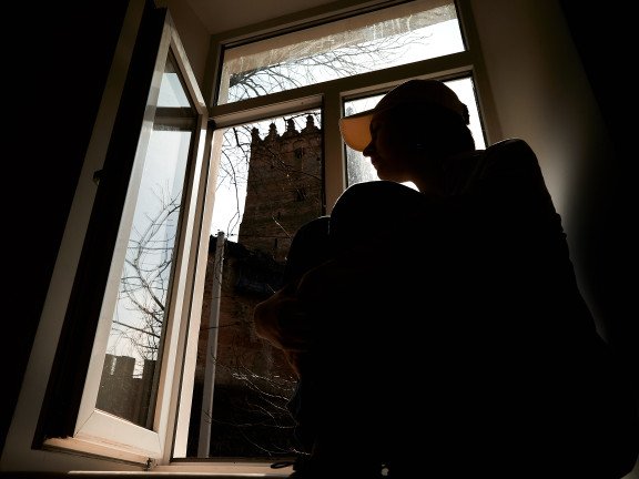 Силует дівчини на на підвіконні з видом на Луцький замок з вікна.