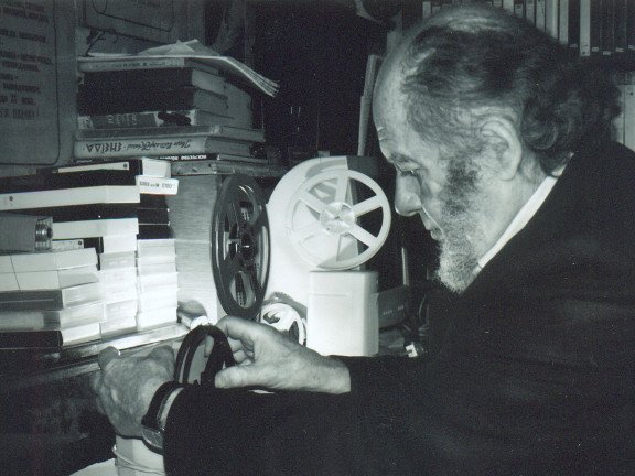 Сивий чоловік біля стосу книг з кіноплівкою в руках
