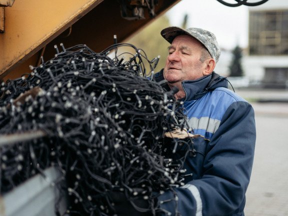 Літній чоловік у спецодязі несе оберемок гірлянд.