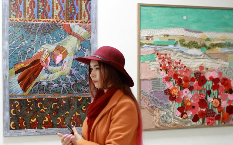 Дівчина в червоному капелюсі та помаранчевому пальто на тлі картин.