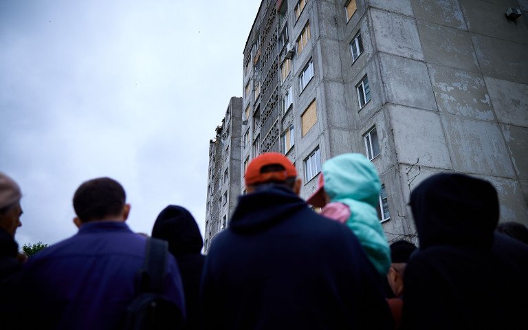 Люди стоять навпроти зруйнованої багатоповерхівки.