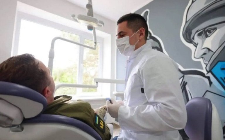 військовослужбовець у стоматологічному кріслі та стоматолог в білому халаті та масці