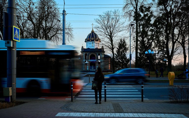 Динамічна вулиця з громадським транспортом, людьми та церквою на горизонті.