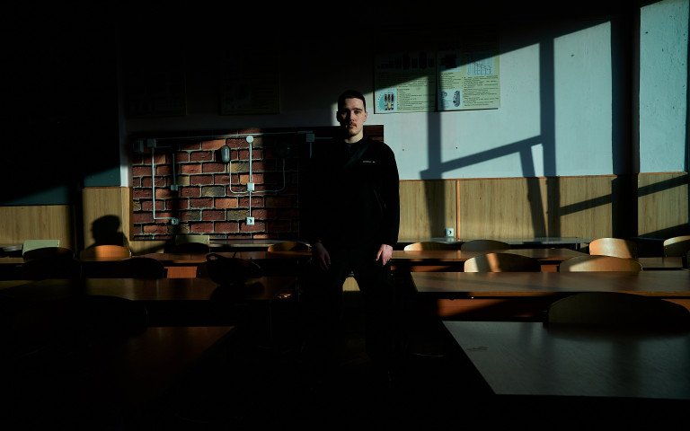 У центрі класної кімнати з партами стоїть хлопець.