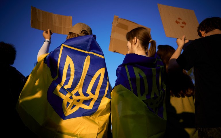 люди з прапорами на плечах з картонками в руках