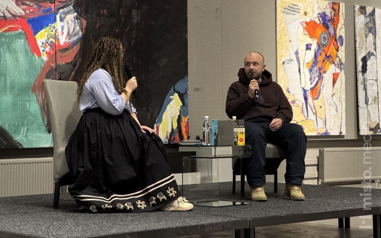 Двоє людей сидять на кріслах на сцені.