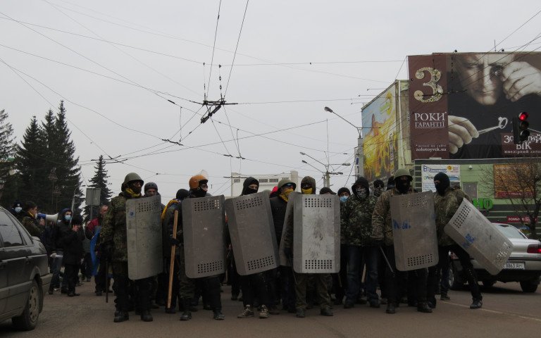 Чоловіки в балаклавах, касках та з міліцейськими металевими щитами стоять на проїжджій частині проспекту Волі у Луцьку.